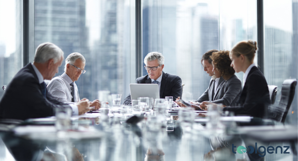 A group of six focused executives in formal business attire sitting around a long, glass conference table in a bright, modern high-rise office.