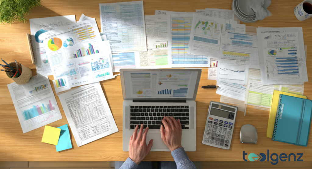 Overhead view of a wooden desk covered in financial documents, charts, a laptop, and a calculator.