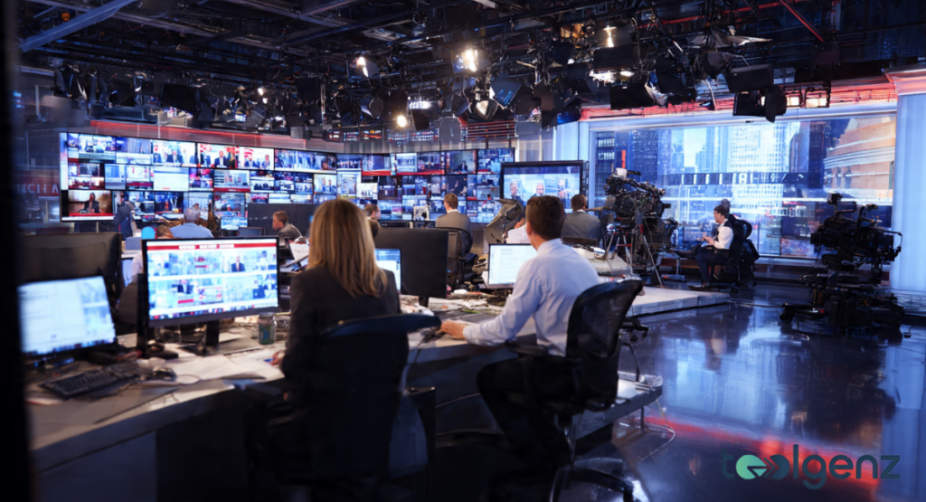 A busy news studio with anchors and crews at work, surrounded by multiple screens displaying live broadcasts. The screens show news feeds, interviews, and breaking headlines, covering political events.